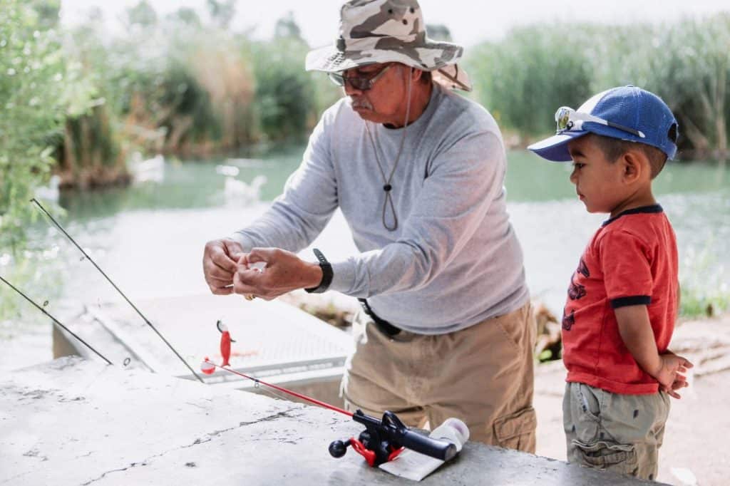 Grand parent teaching grandson to fish at camp site